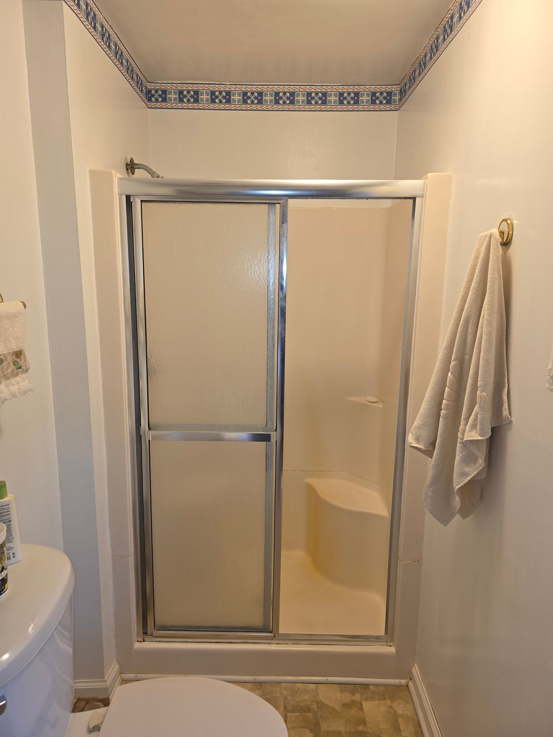 Shower stall with sliding glass doors and a built-in seat, in a bathroom.