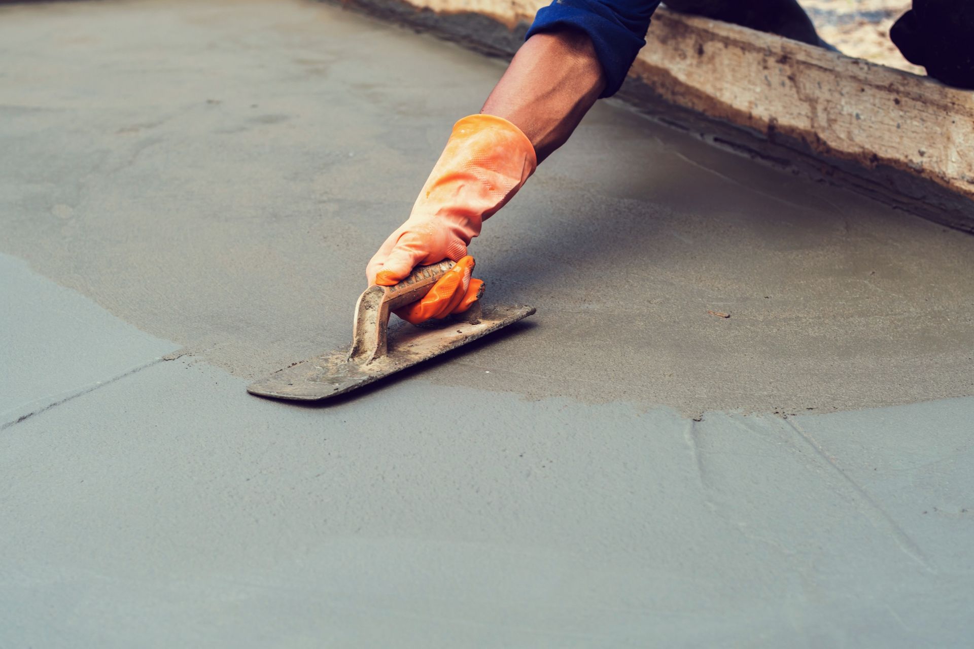 Worker smoothing wet concrete with a trowel on a sidewalk edge