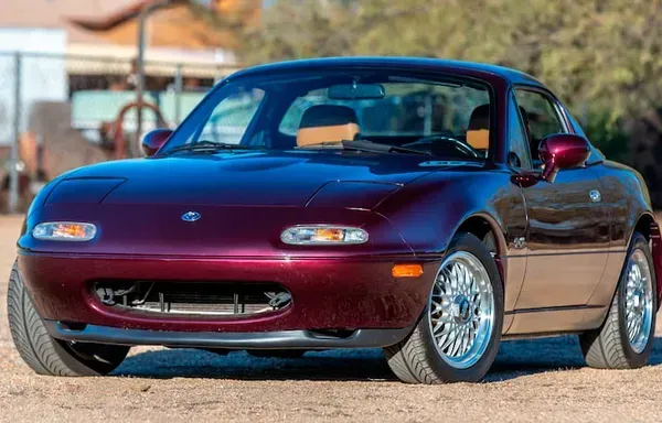 Bourgondische Mazda Miata roadster met chromen velgen, geparkeerd op een onverharde weg.