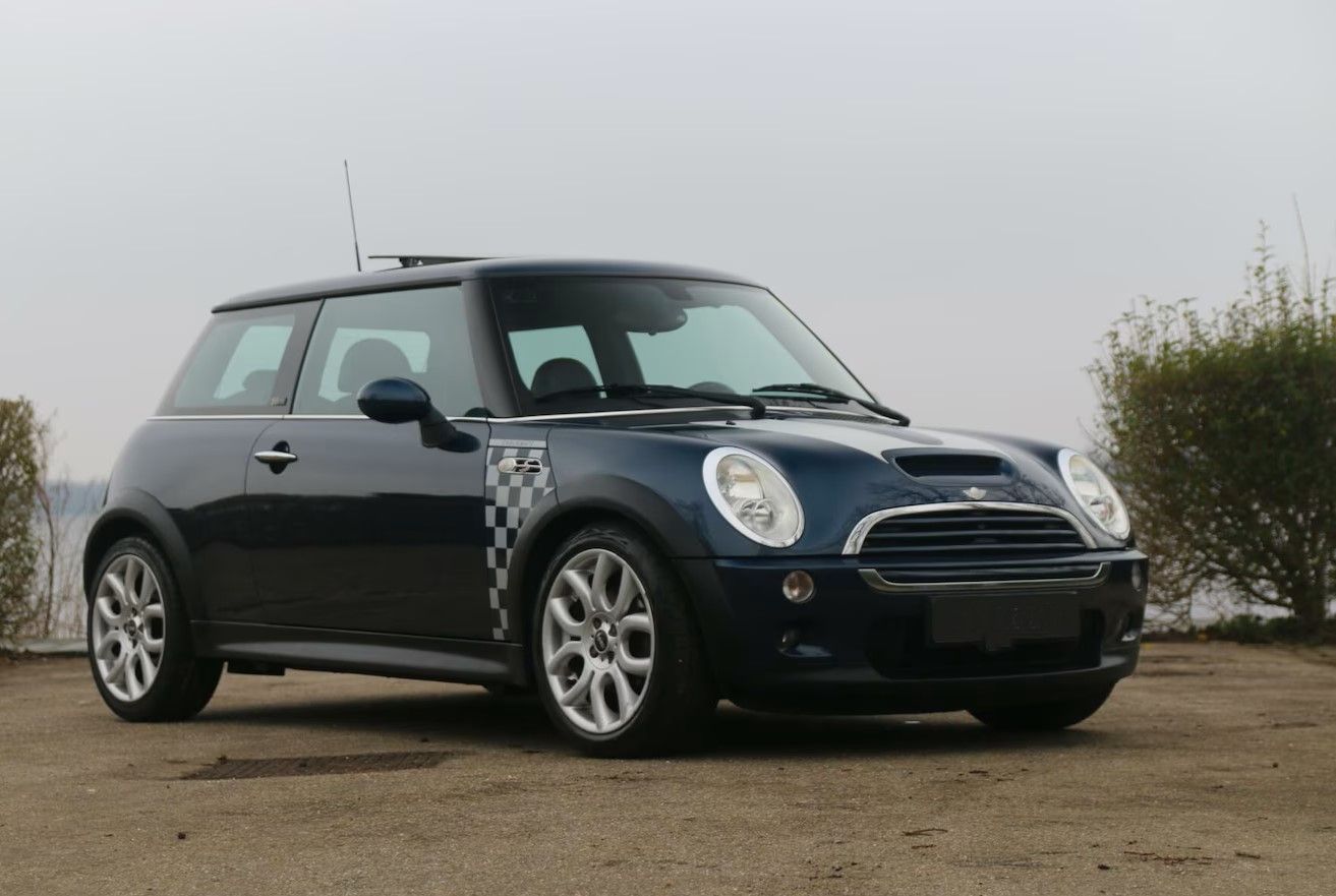 Donkerblauwe Mini Cooper met detail van de geblokte vlag, geparkeerd op zand.