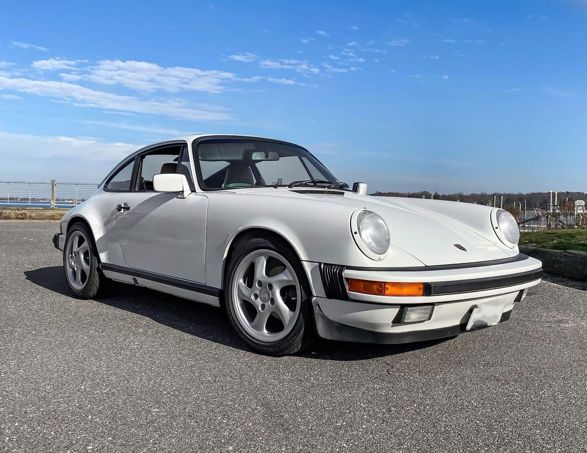 Witte Porsche 911 coupé geparkeerd op asfalt, met een blauwe lucht op de achtergrond.
