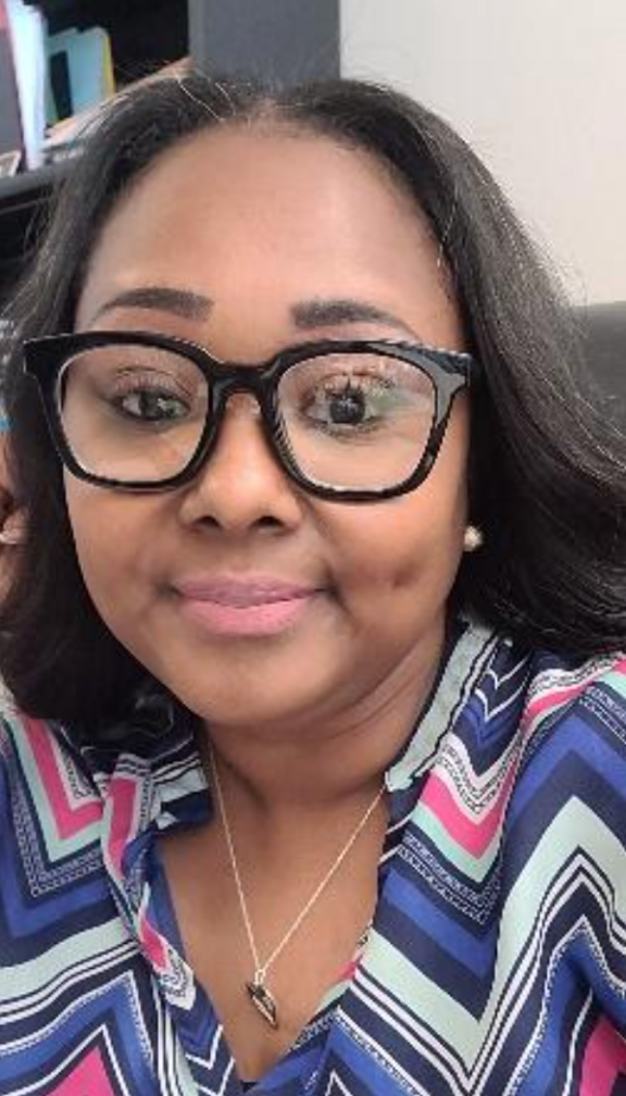 A woman wearing glasses and a necklace is smiling for the camera.