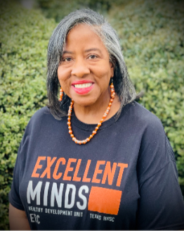 A woman wearing a yellow shirt and a blue dress is standing with her hands on her hips.