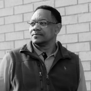 A man in a suit is sitting on a chair with his hands on his hips.