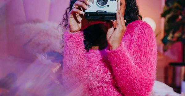 A woman in a pink sweater is taking a picture of herself with a camera.