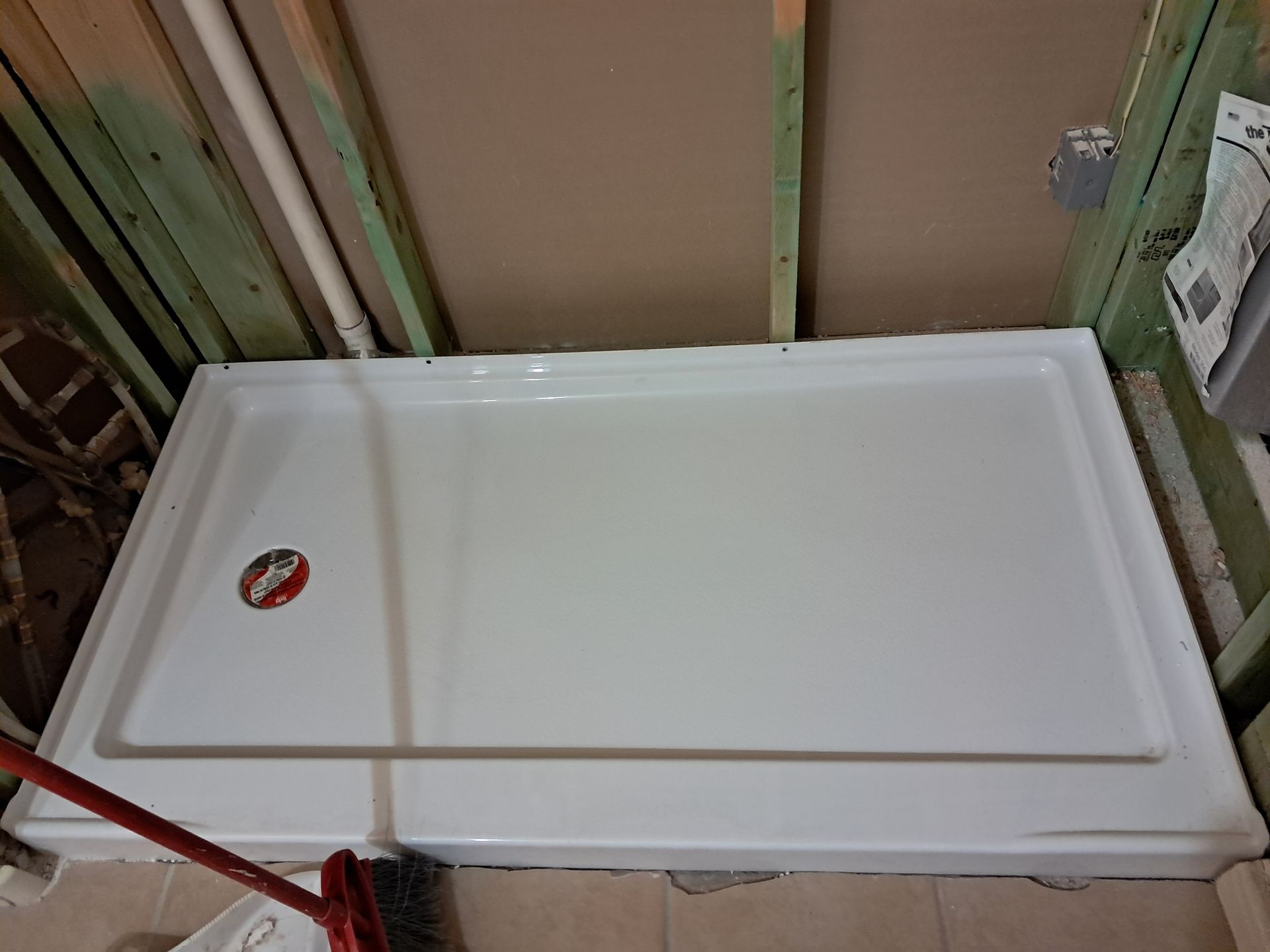 White rectangular shower base installed in a partially constructed bathroom, surrounded by wood framing.