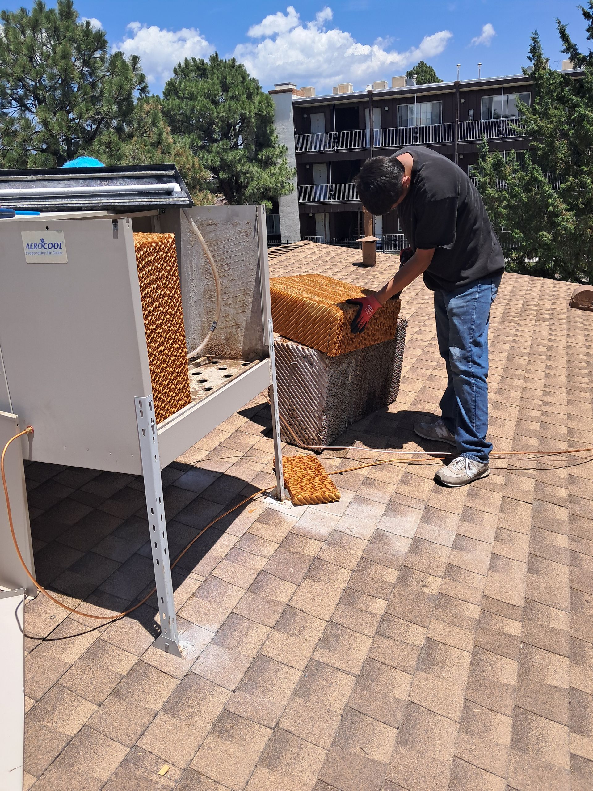 Three large, gray air conditioning units mounted on legs outside a greenhouse.