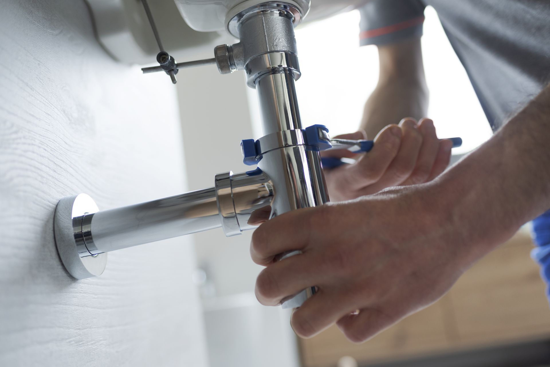 Person using tools to assemble plumbing under a sink.
