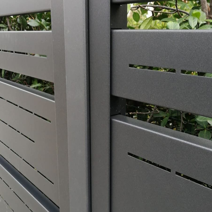 Vista ravvicinata di una recinzione per la privacy in metallo grigio scuro opaco con lamelle orizzontali caratterizzate da strette aperture rettangolari.