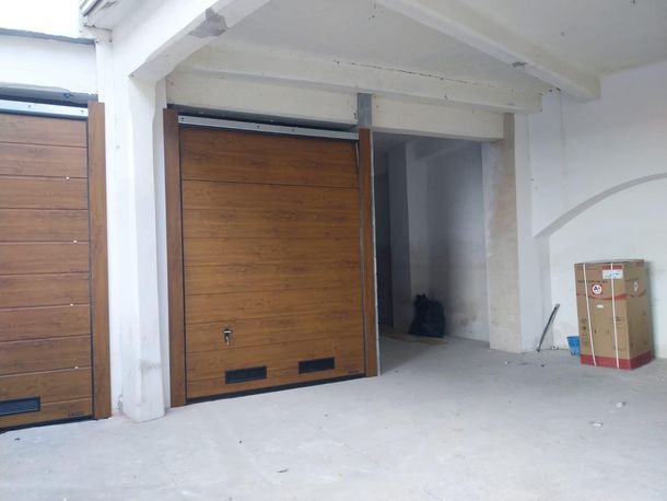 Due portoni da garage orizzontali marroni in uno spazio industriale chiaro e non rifinito, con un box nell'angolo.