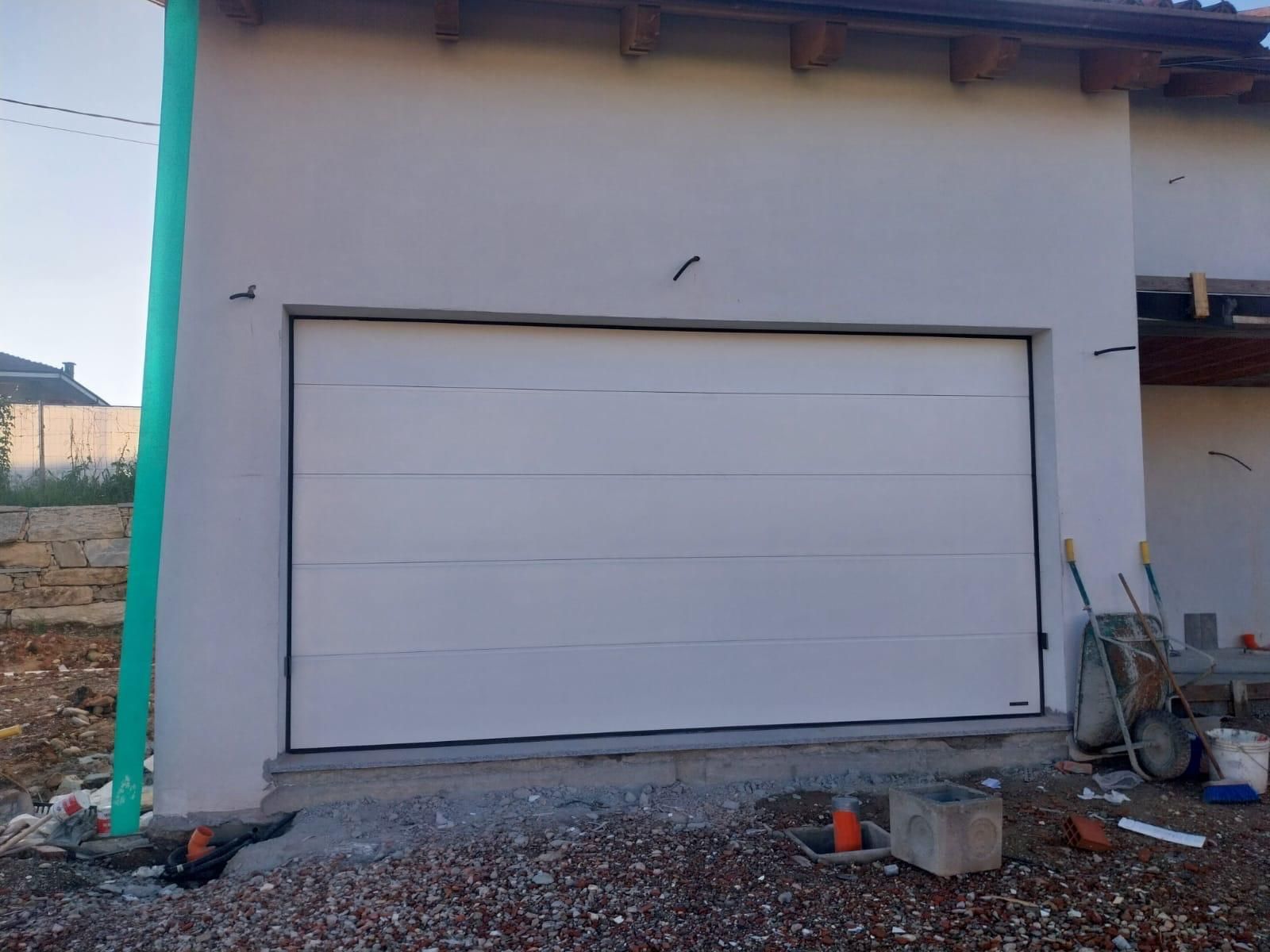 Una moderna porta da garage sezionale bianca a pannelli multipli, installata sulla facciata di un edificio di colore chiaro sotto un cielo sereno.