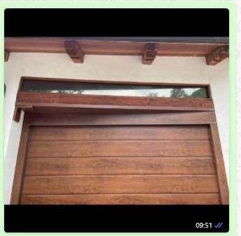 Una porta da garage in legno con una fila superiore di finestre orizzontali, incastonata sotto travi decorative in legno su uno sfondo bianco.