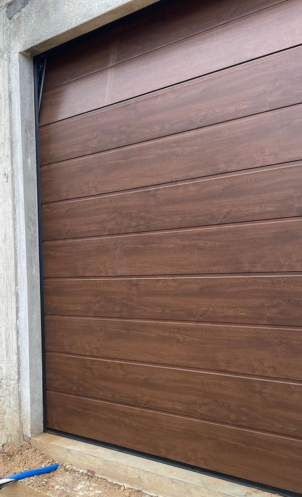 Primo piano di una porta da garage marrone a pannelli orizzontali, inserita in una cornice di cemento di colore chiaro.