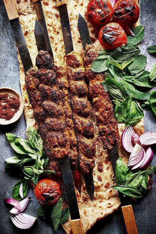 A close up of a kebab on a cutting board with vegetables.
