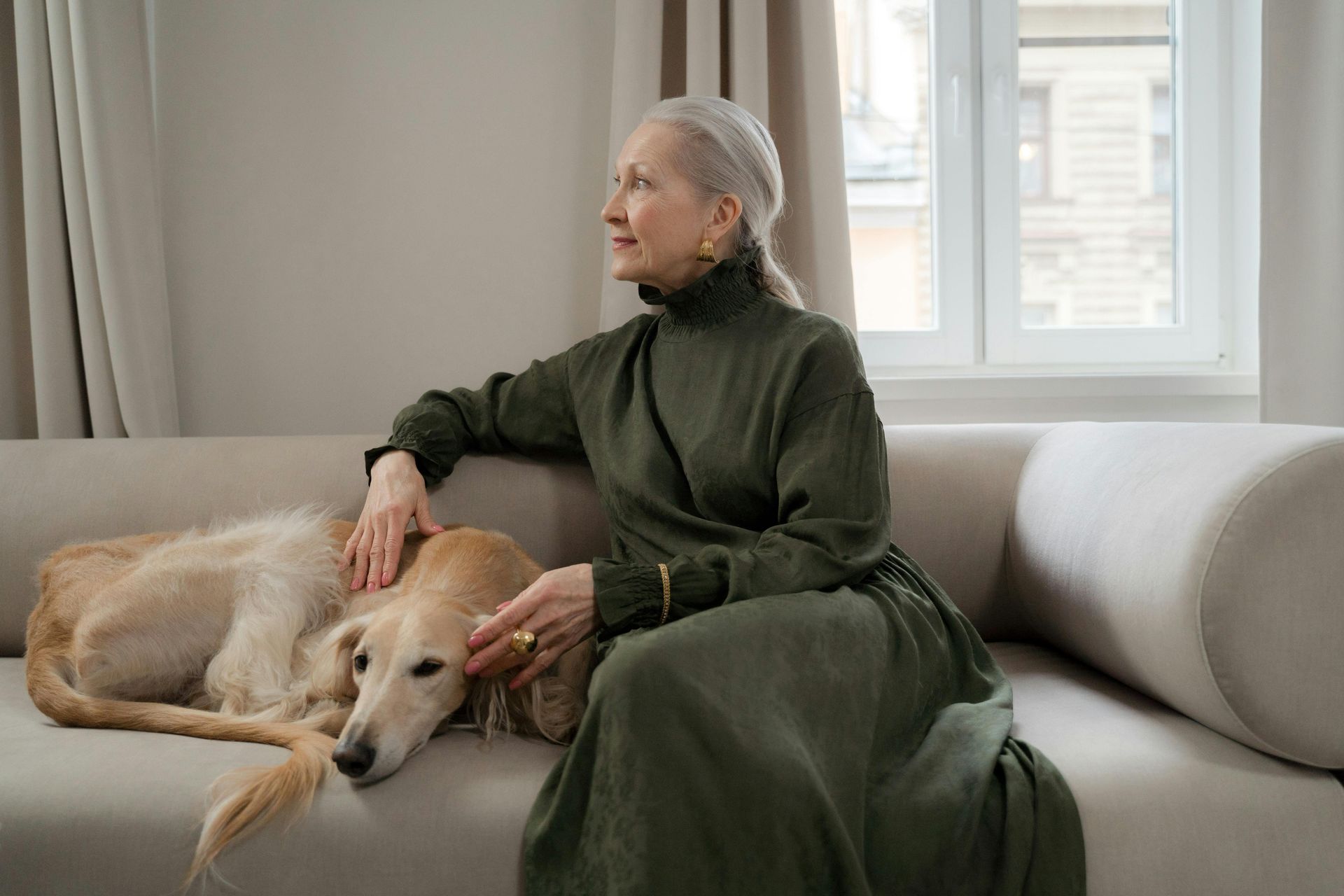 An elderly woman is sitting on a couch with a dog.