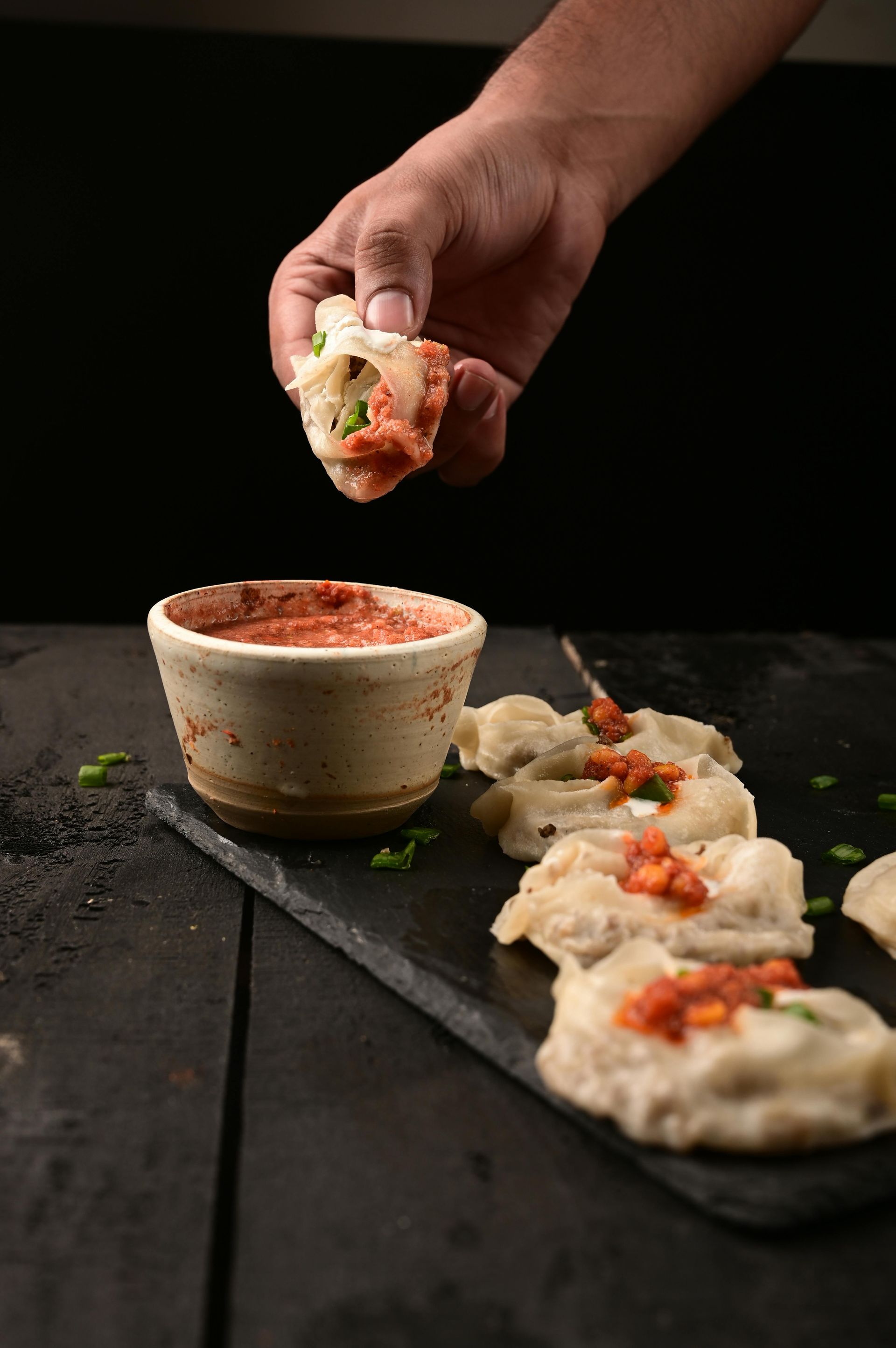 A person is dipping a dumpling into a bowl of sauce.