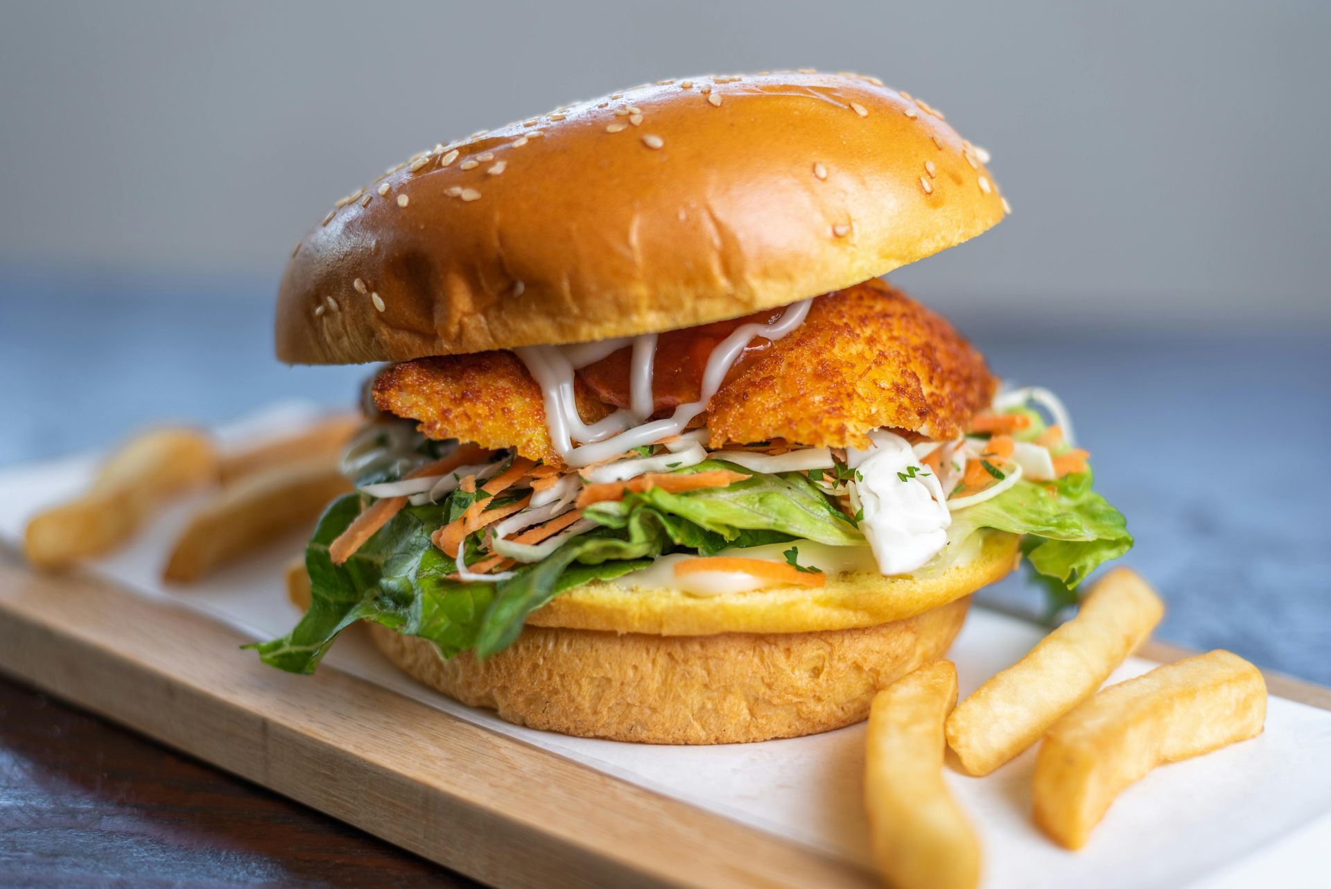 A chicken sandwich is sitting on a wooden cutting board next to french fries.