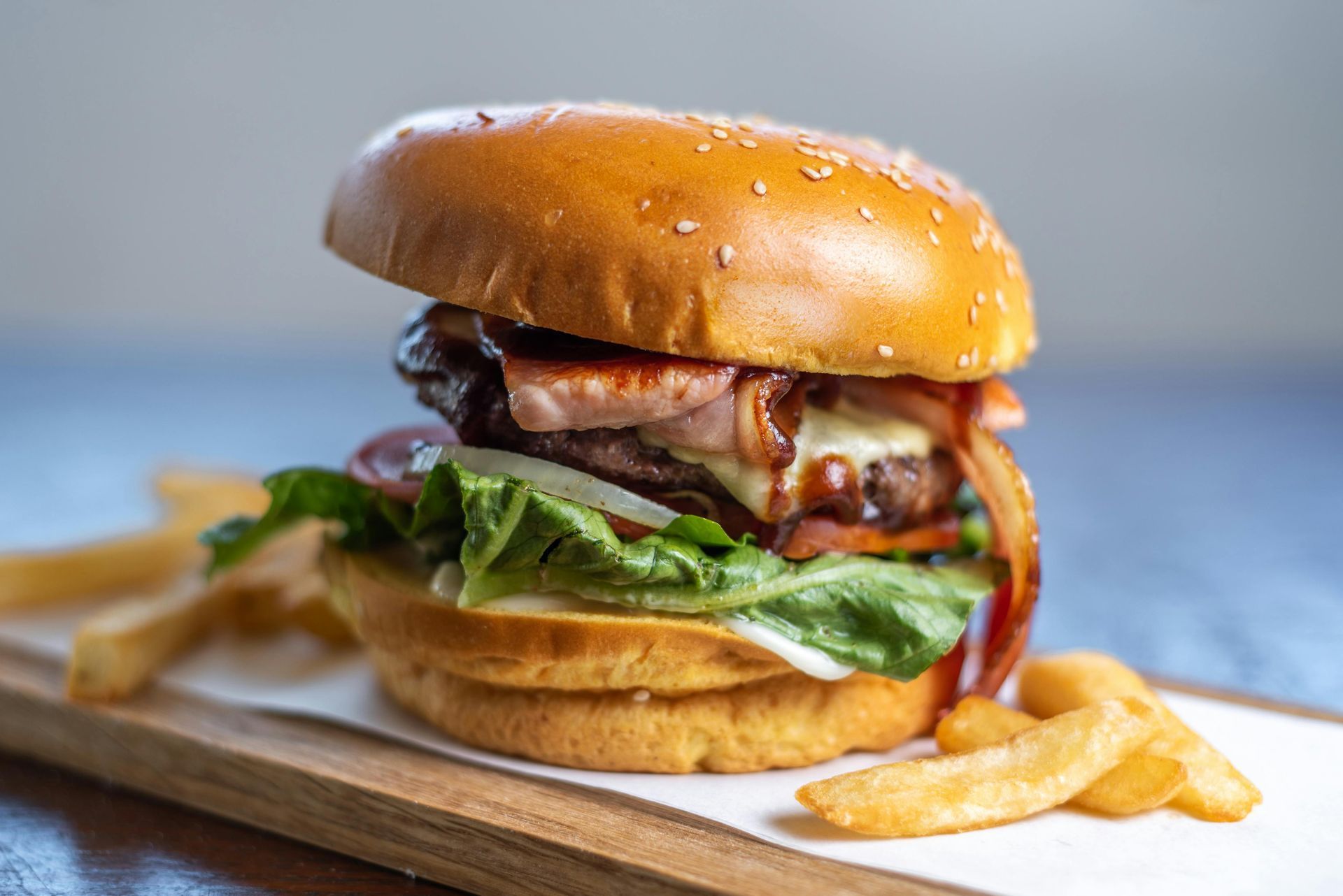 A hamburger is sitting on a wooden cutting board next to french fries.