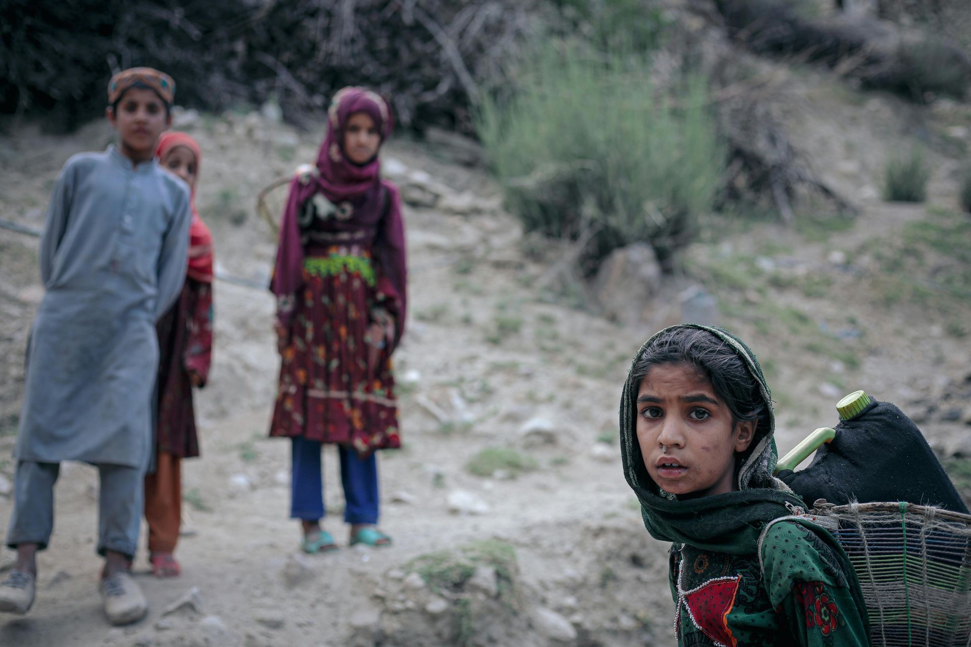 A group of children are standing next to each other on a dirt road.