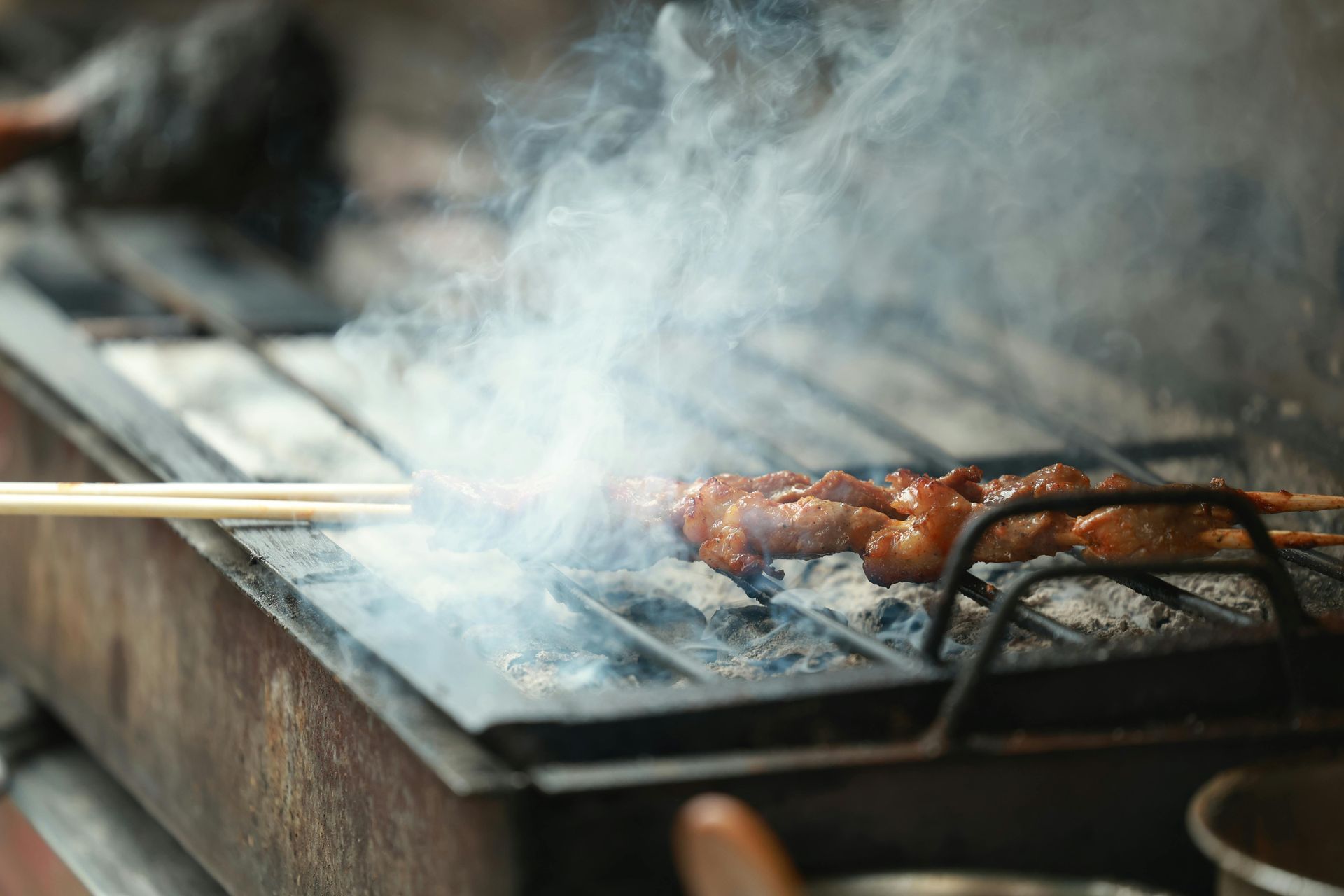 A person is cooking meat on a grill with chopsticks.