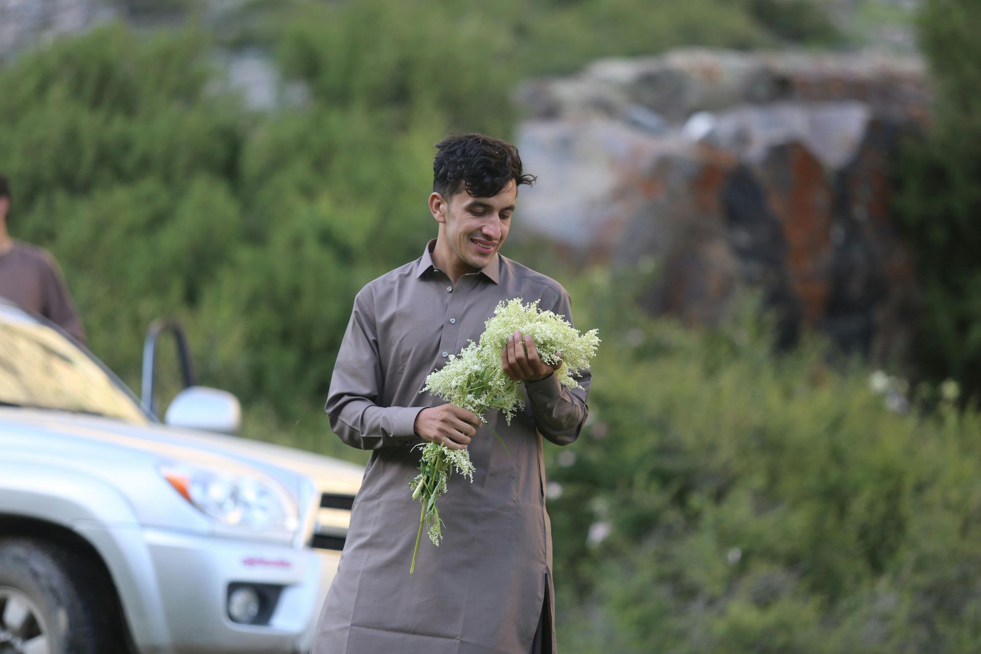 A man is holding a bouquet of flowers in front of a car.