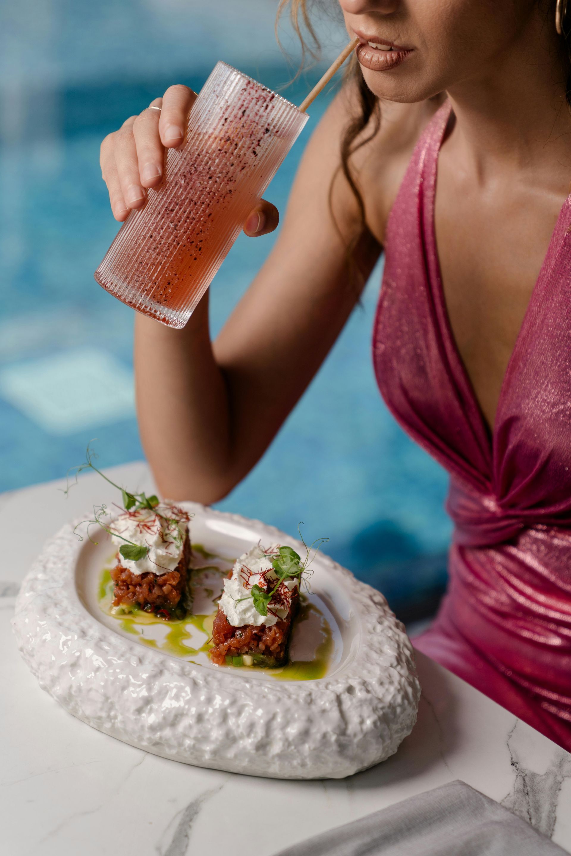 A woman in a pink dress is drinking a drink from a glass with a straw.