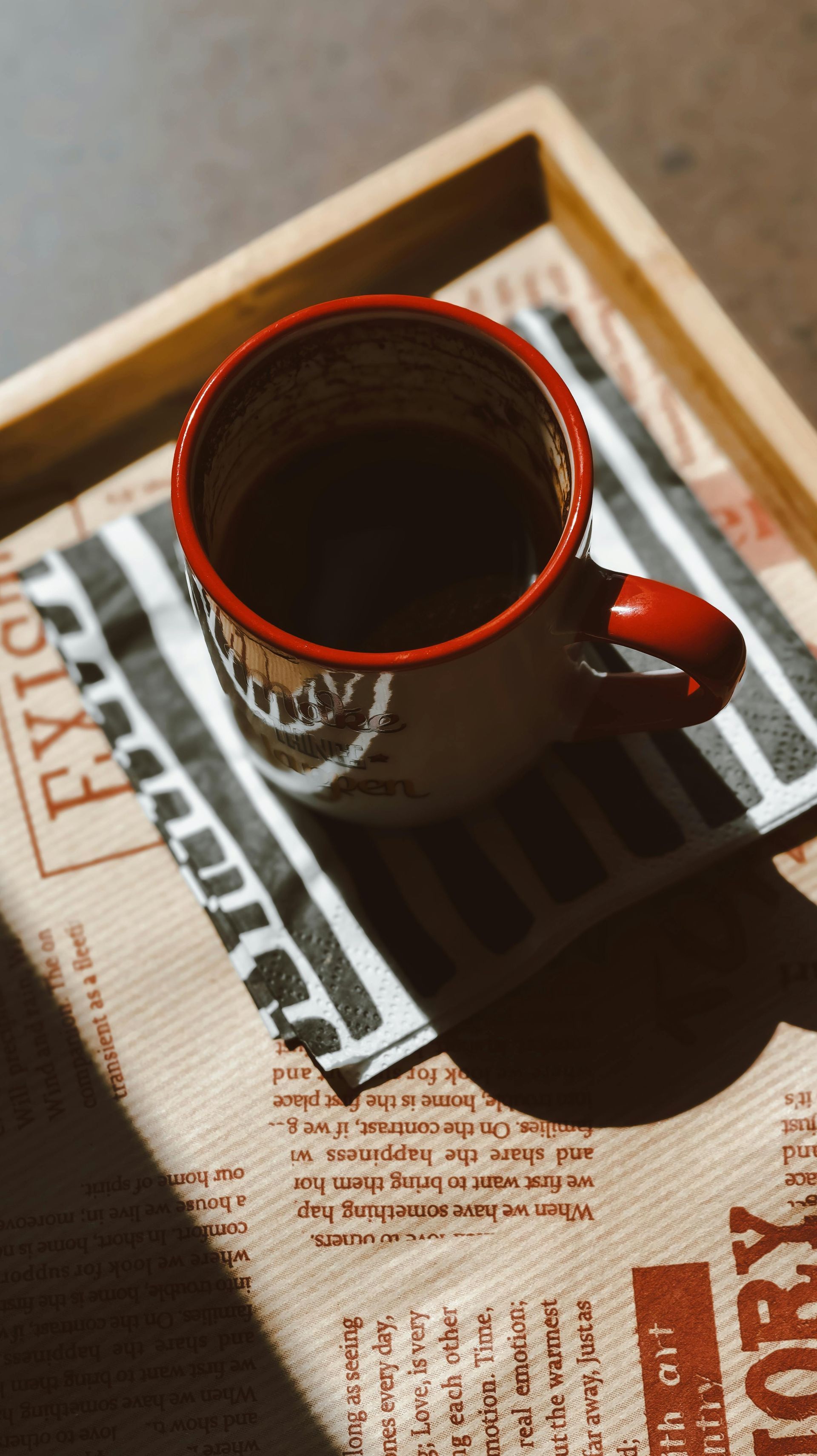 A cup of coffee is sitting on top of a newspaper on a tray.