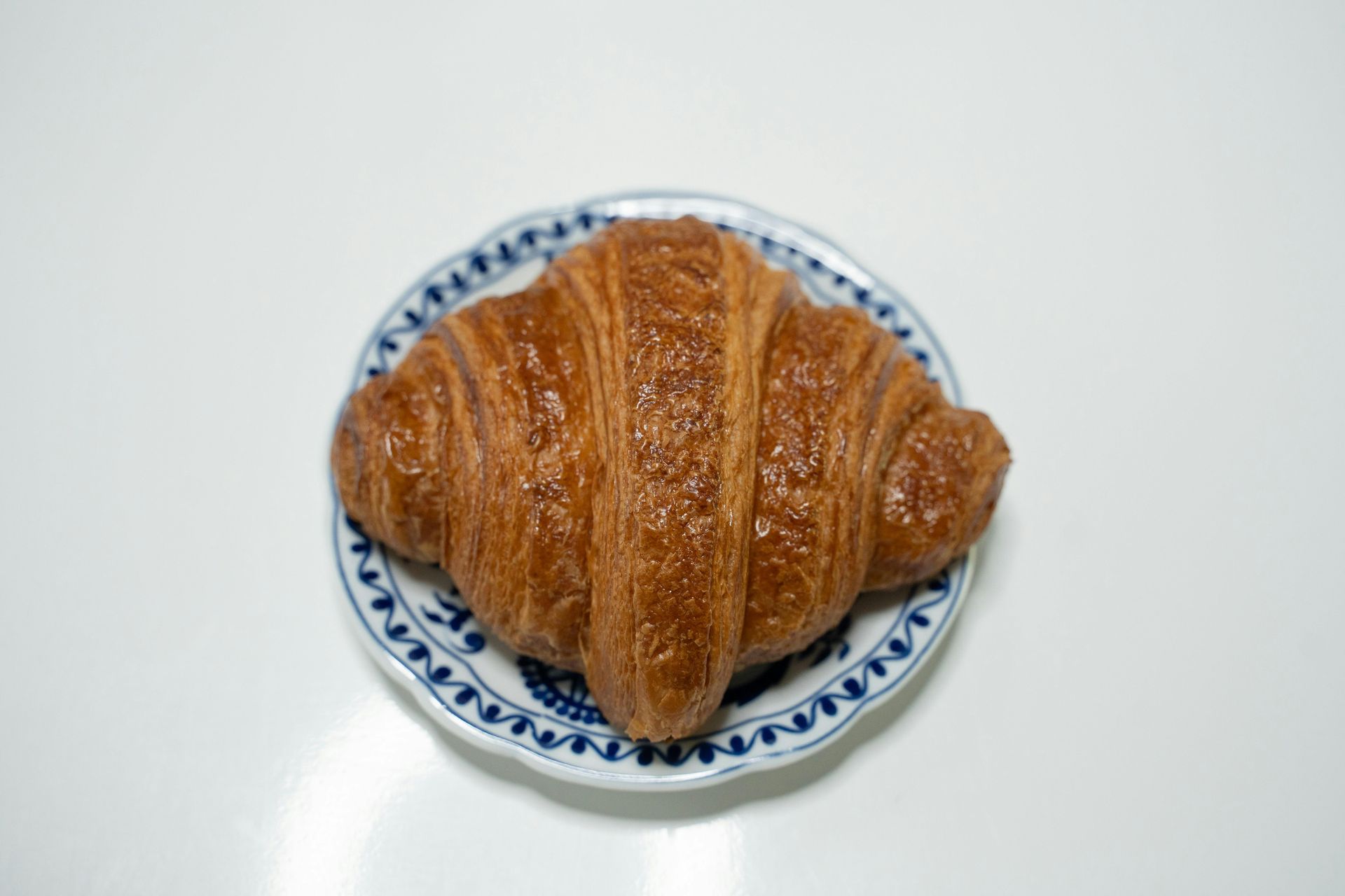 A croissant is sitting on a blue and white plate on a table.