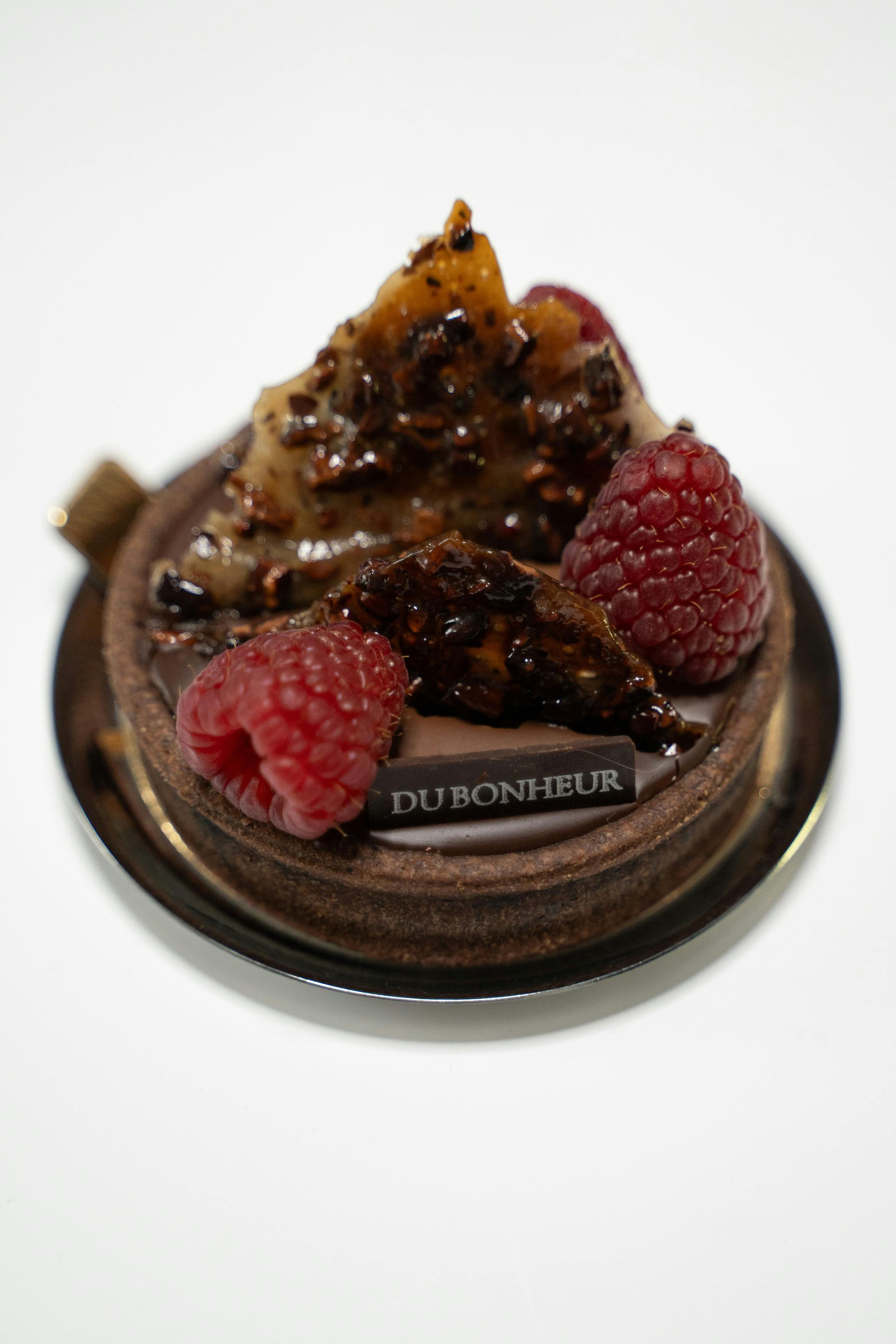 A small chocolate cake with raspberries and nuts on top