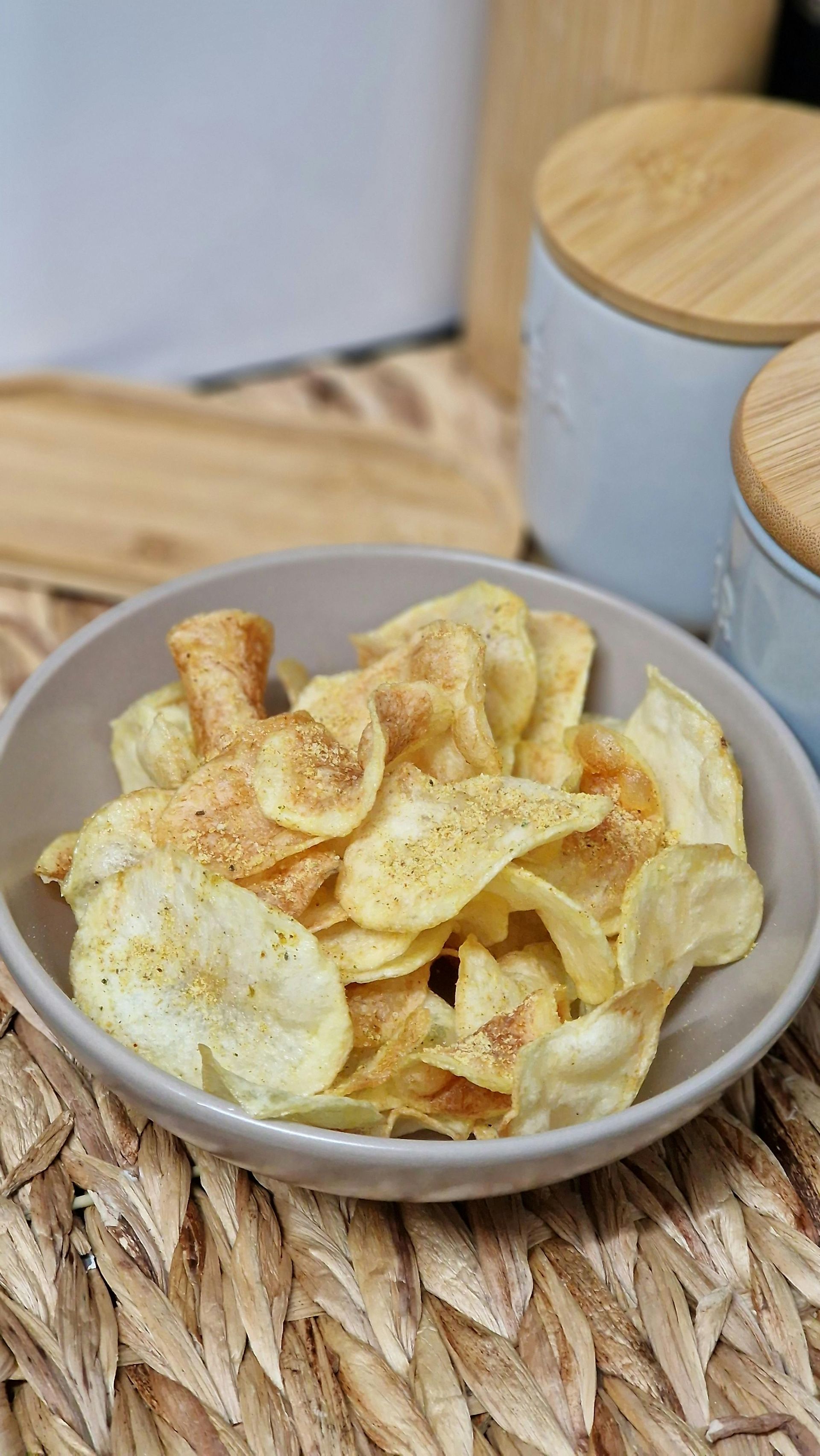 A bowl of potato chips is sitting on a wicker mat on a table.