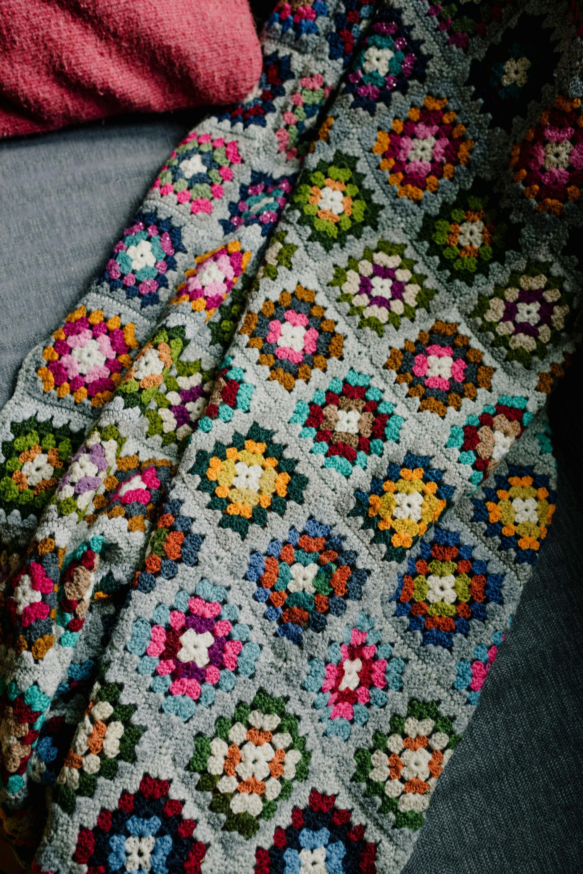 A close up of a colorful crocheted blanket on a bed.