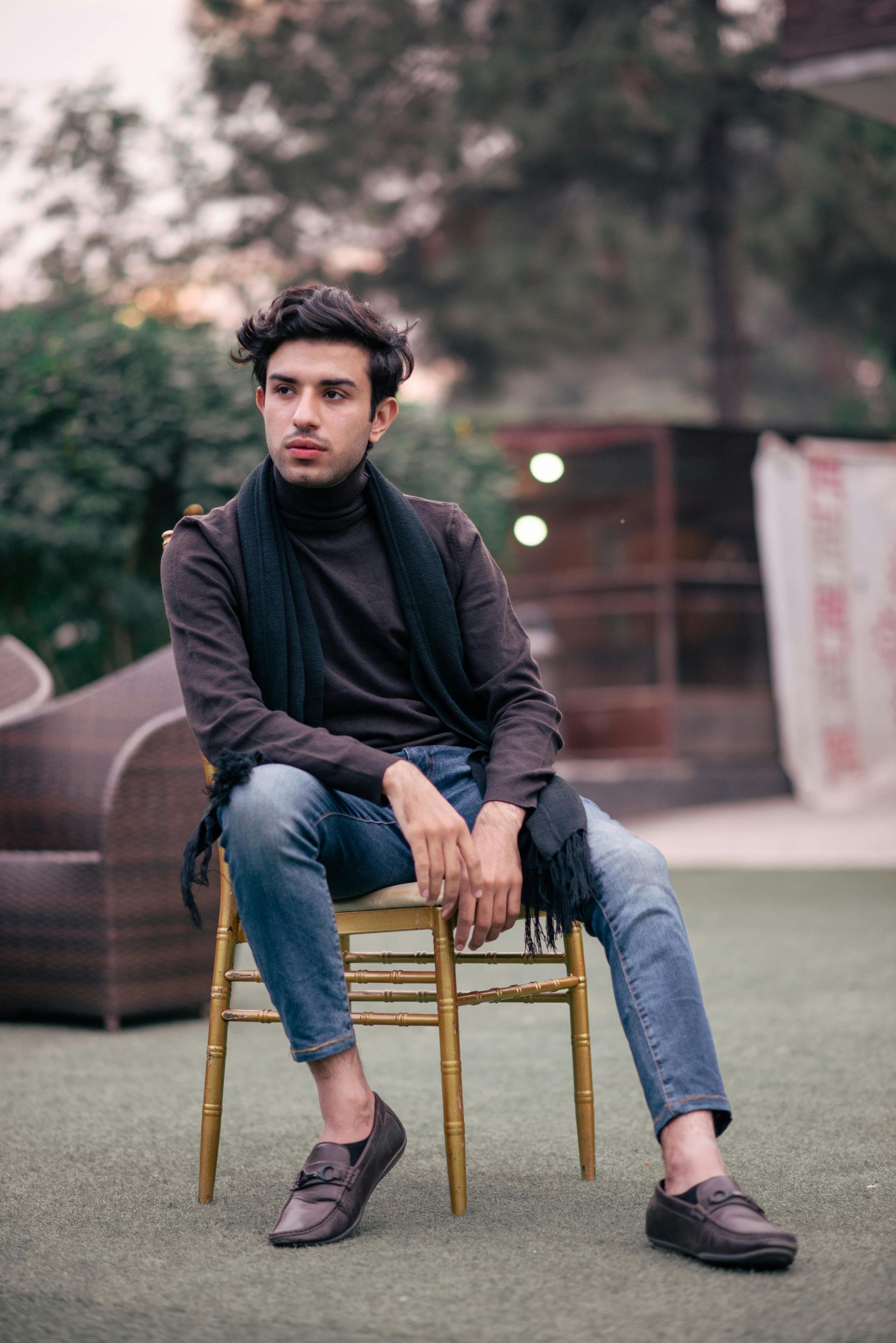 A young man is sitting on a chair with his legs crossed.