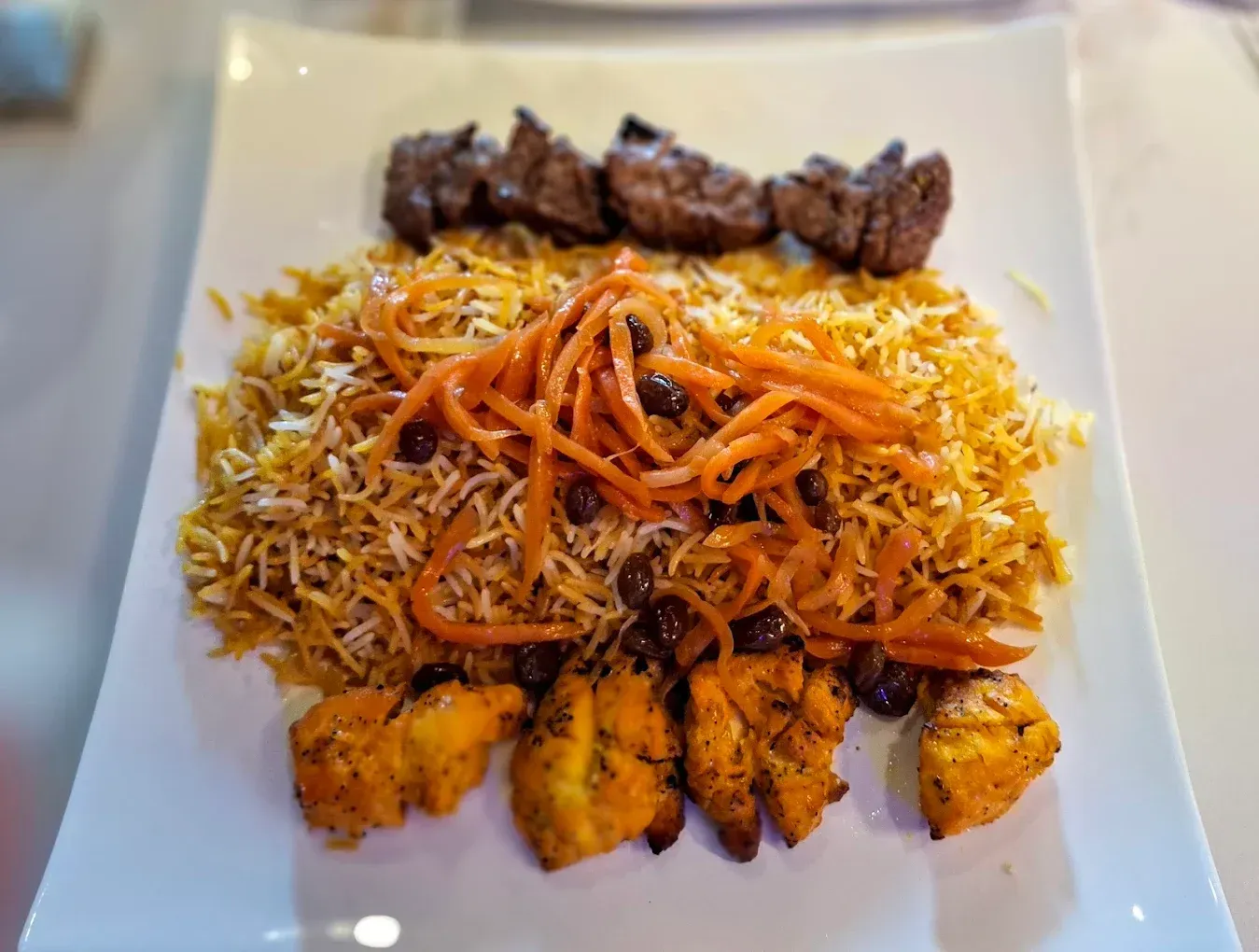 A white plate topped with rice , meat , carrots and raisins.