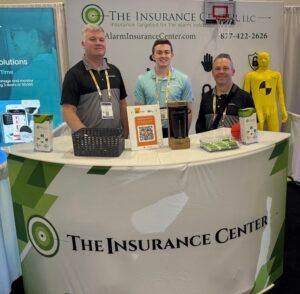 Three people stand behind a branded counter for The Insurance Center at a trade show booth, with a dummy visible nearby.