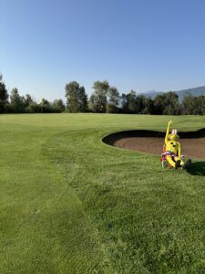 A yellow crash test dummy figure sits in a sand bunker on a green golf course under a clear blue sky.