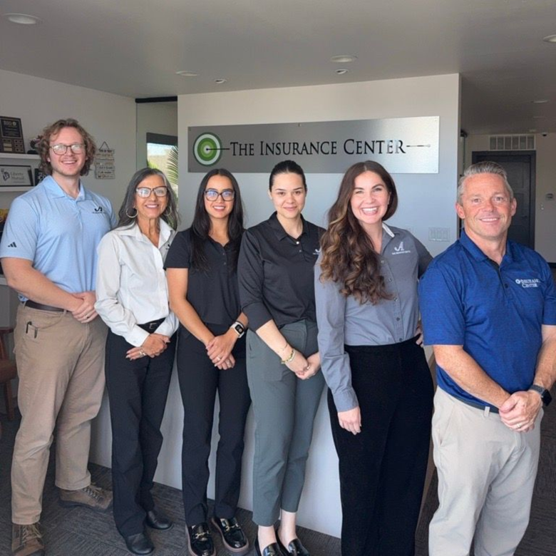 City skyline at sunset with a backdrop of mountains and a foreground of lush, green trees and residential houses.