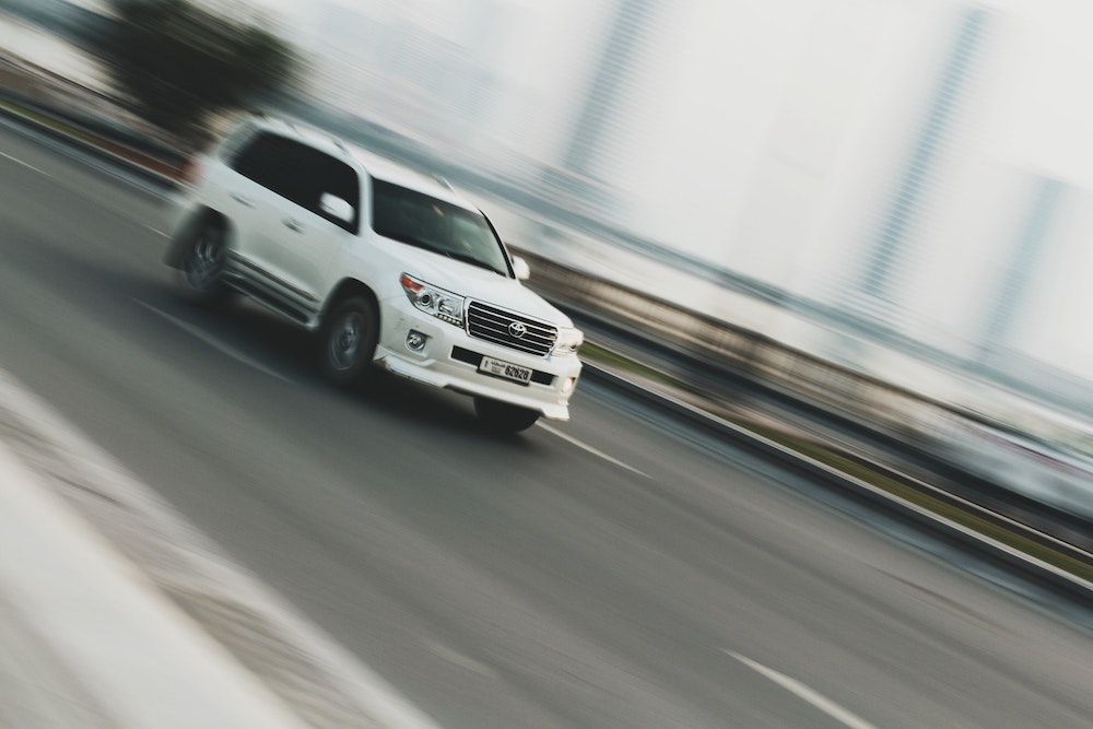 A white SUV driving on a highway with motion blur, emphasizing speed.