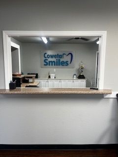 A woman in a dentist chair smiles, looking at her teeth in a hand mirror.
