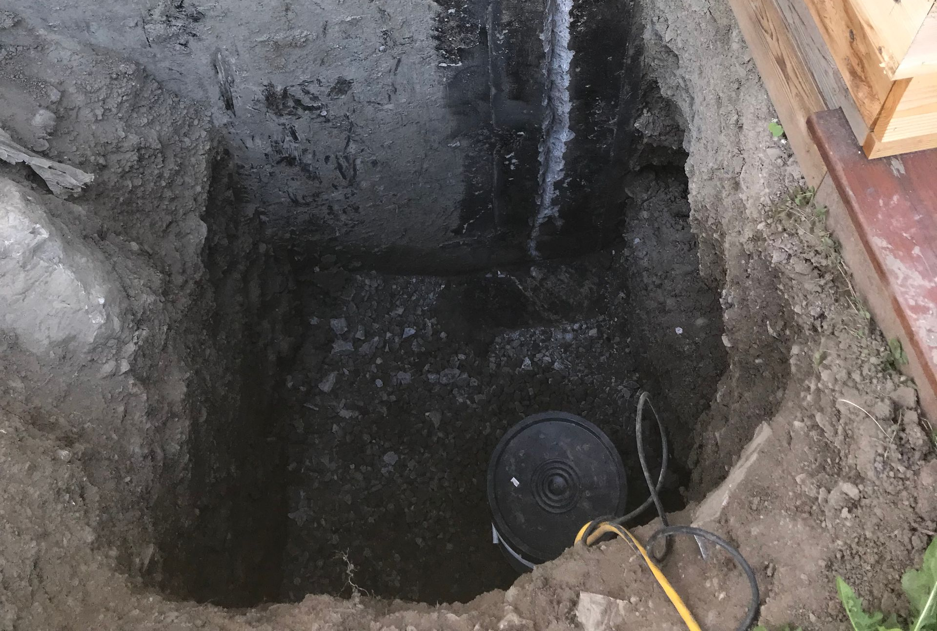 Fosse d'excavation à ciel ouvert avec de l'eau sombre, un tuyau de drainage et un couvercle circulaire noir au fond.