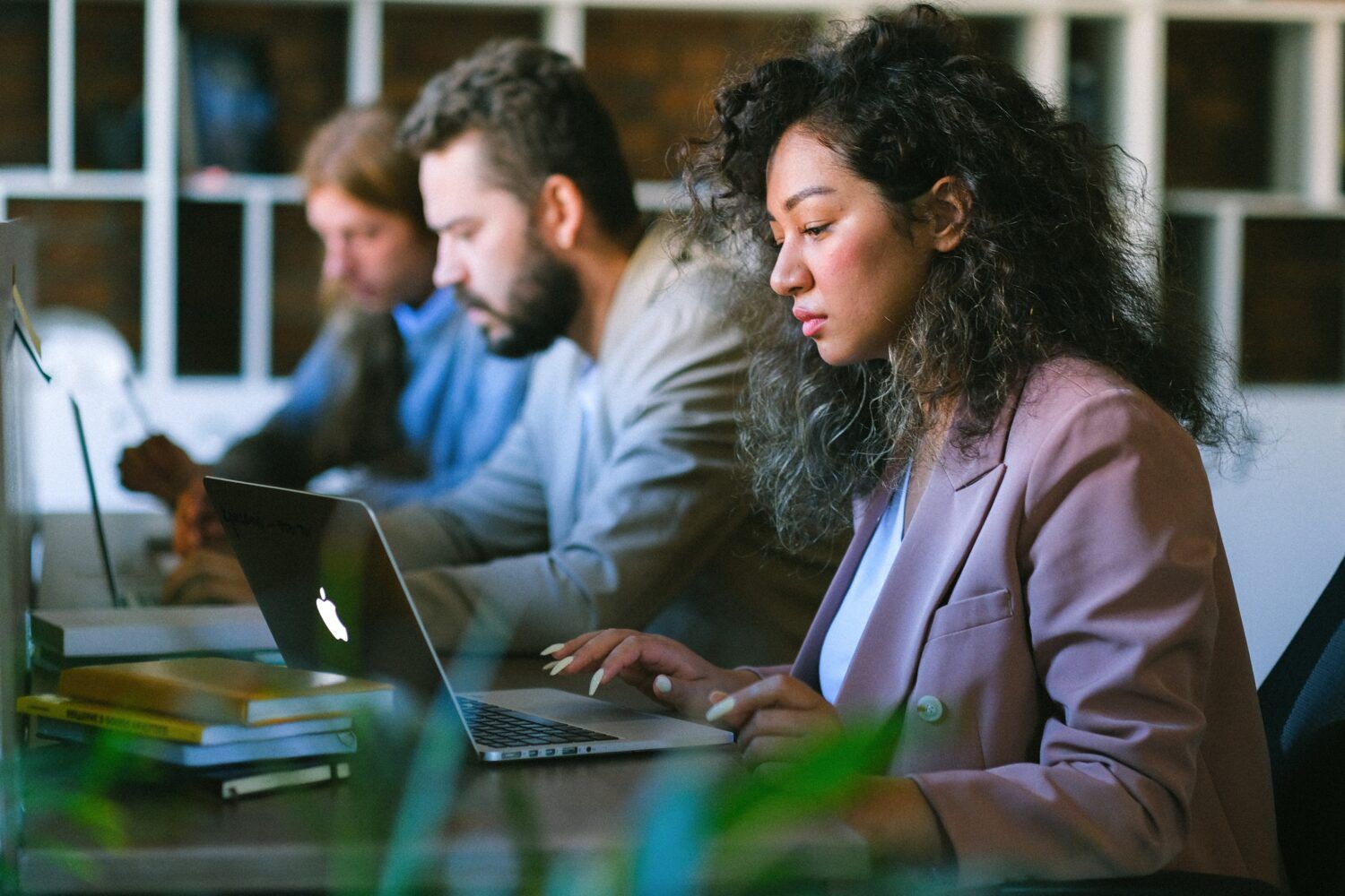 People working on laptops at a table in a modern office, with focused expressions.