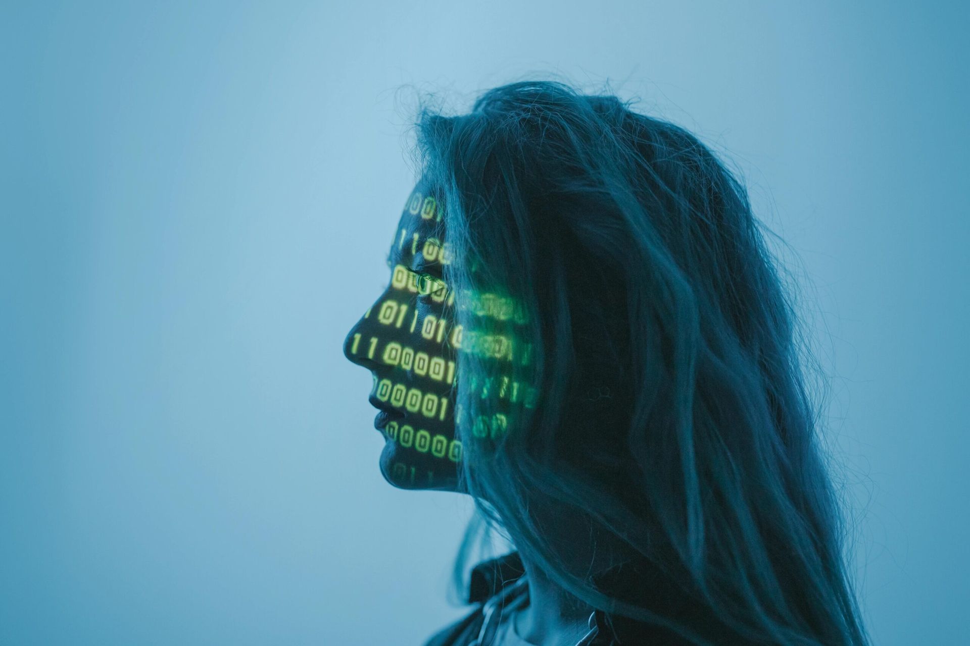 Side profile of a person with glowing green binary code projected on their face against a blue background