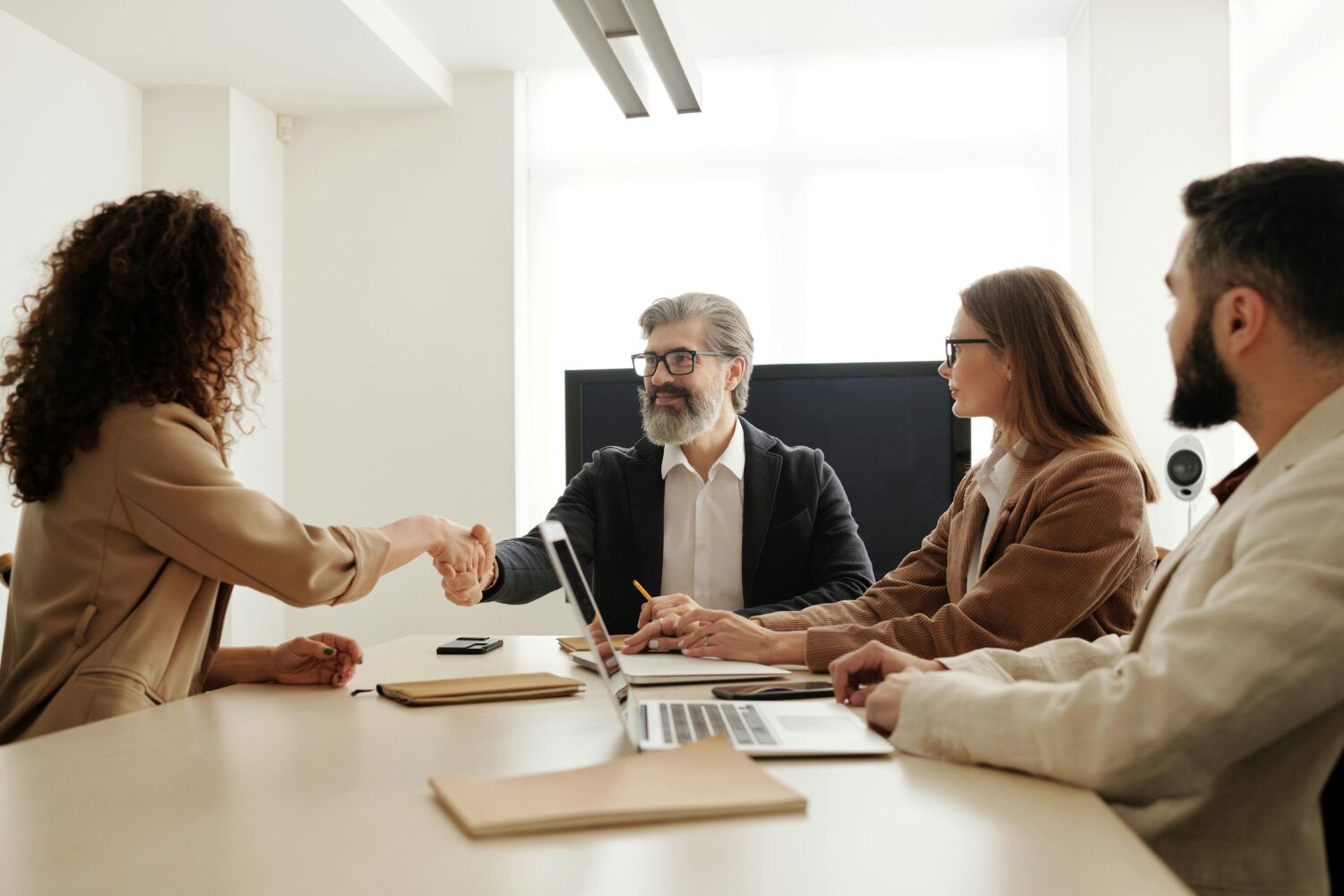 Four colleagues shaking hands across a conference table in a bright office meeting room