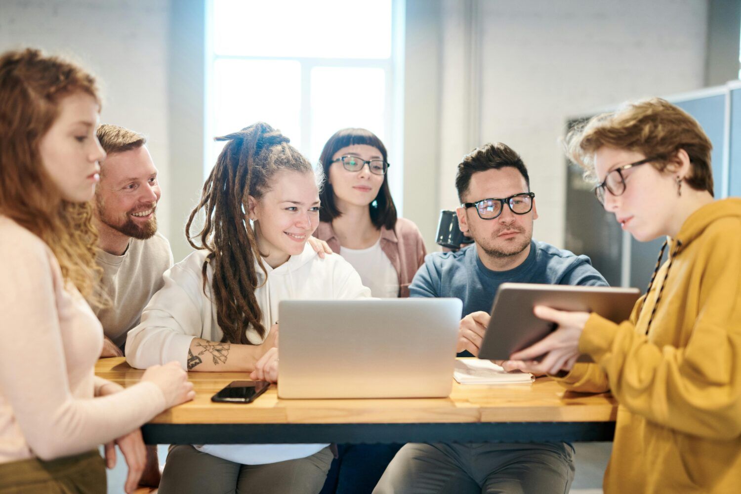 Group of people collaborating around a laptop and tablet at a table in a bright office