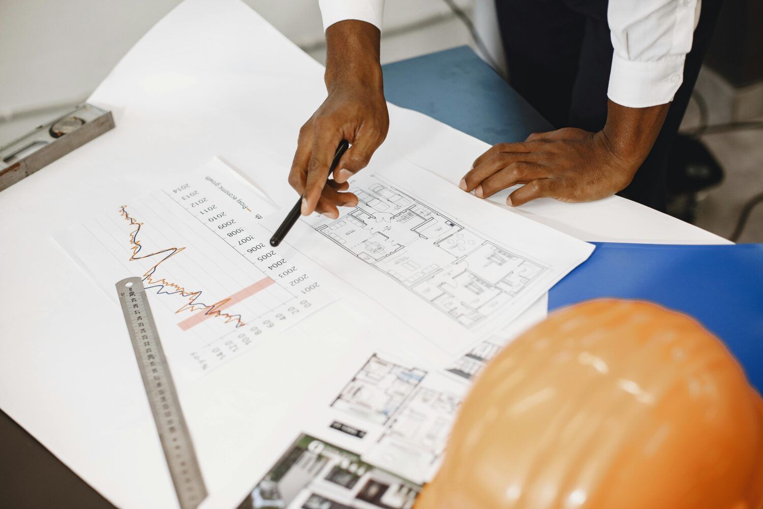 Hands reviewing architectural plans on a desk with a hard hat in the foreground
