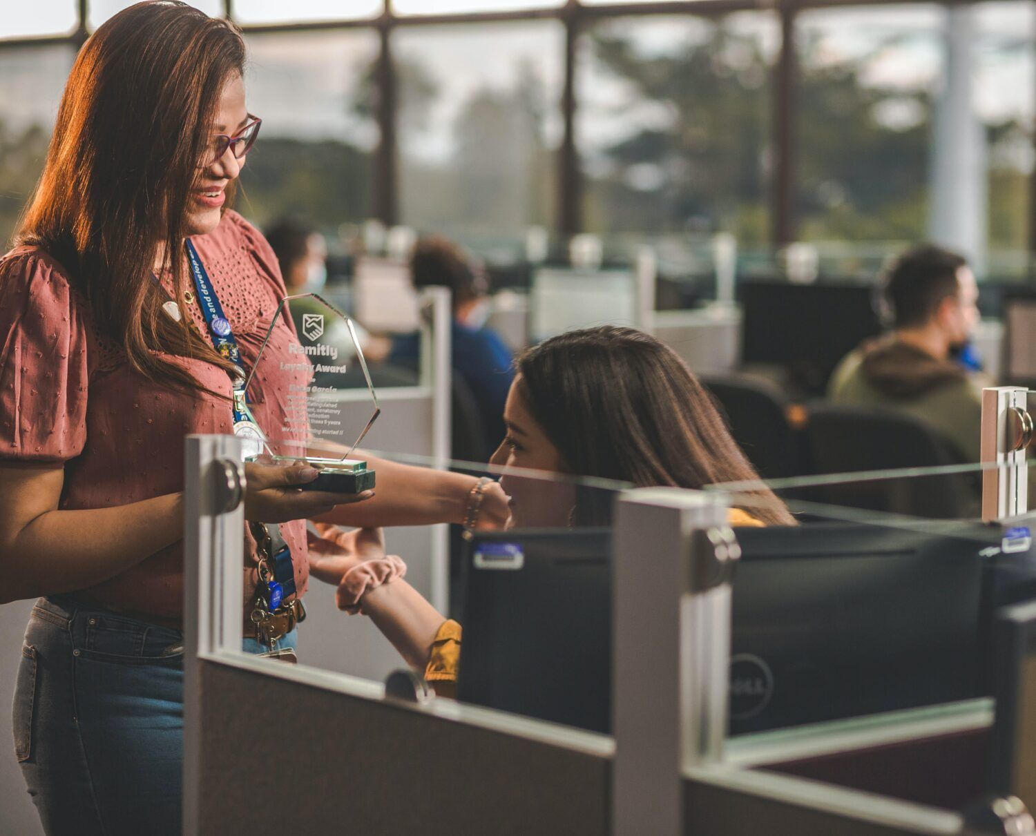 Woman handing an item to a seated coworker in a modern office cubicle