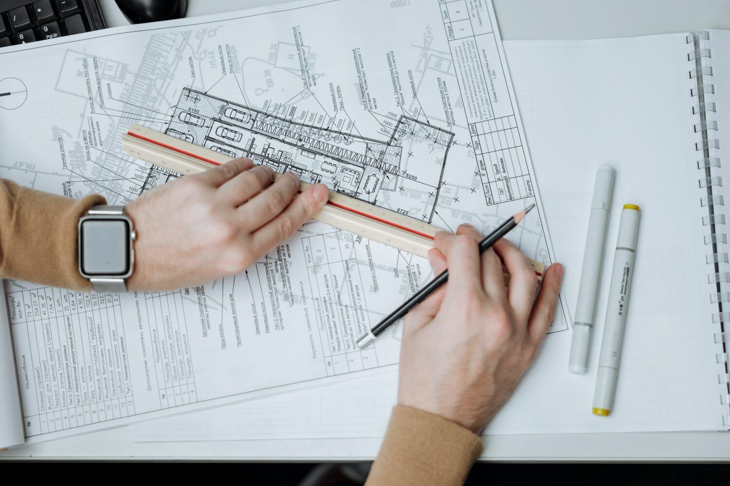 Hands drafting architectural plans with rulers and pencil on a desk