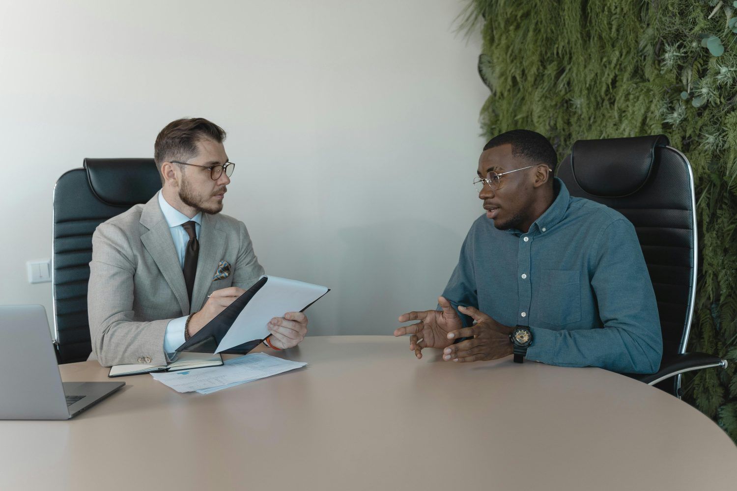 Two people in a meeting across a table, one holding a tablet, in a modern office.