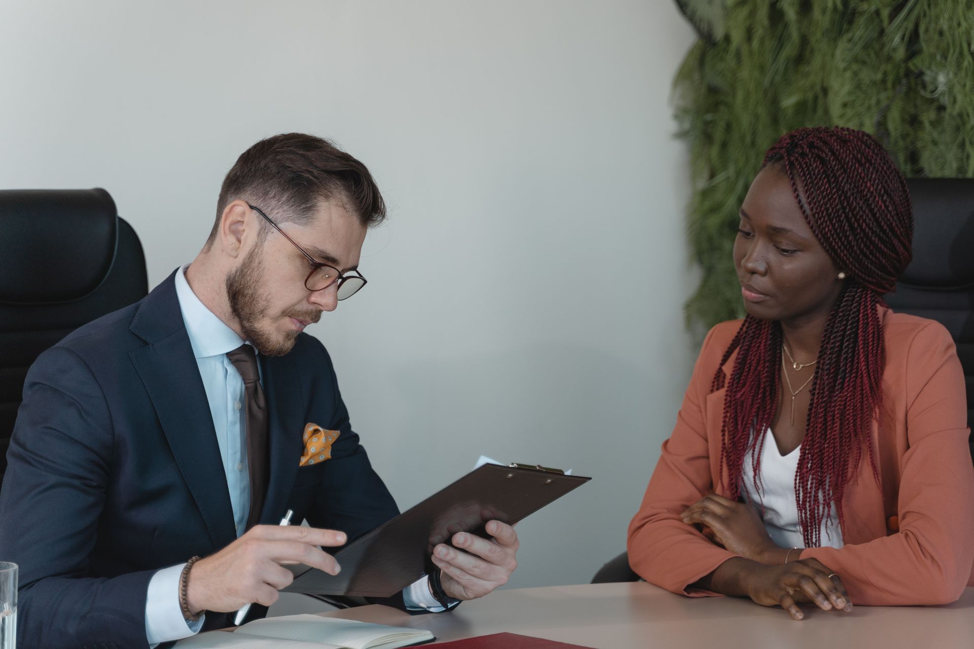 Two people in a meeting reviewing a tablet at a desk, one speaking while the other listens attentively.
