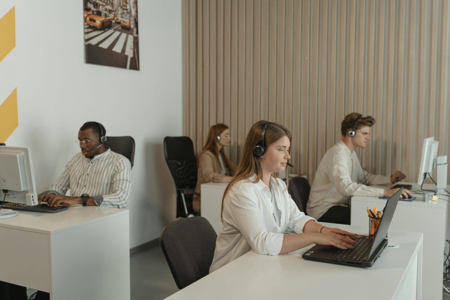 People working at desks with computers in a modern office, including two women wearing headsets