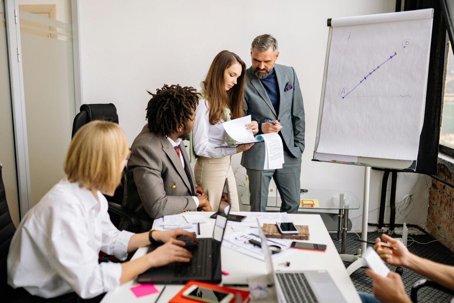 Team meeting in an office, with colleagues discussing notes beside a flip chart and laptop.